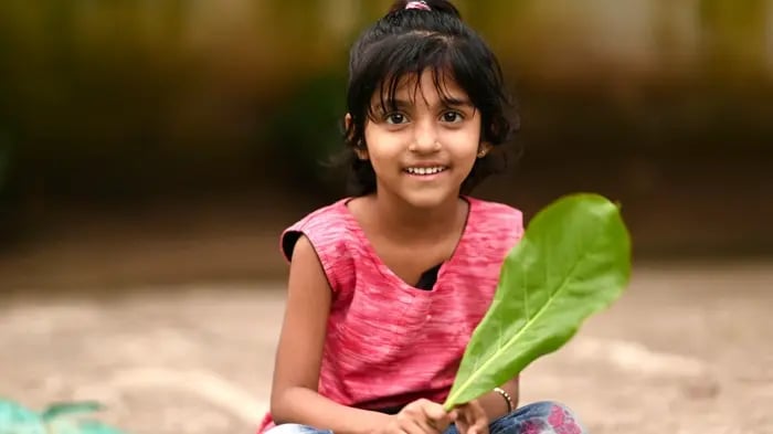 Female Kid Sitting With A Lush Leaf